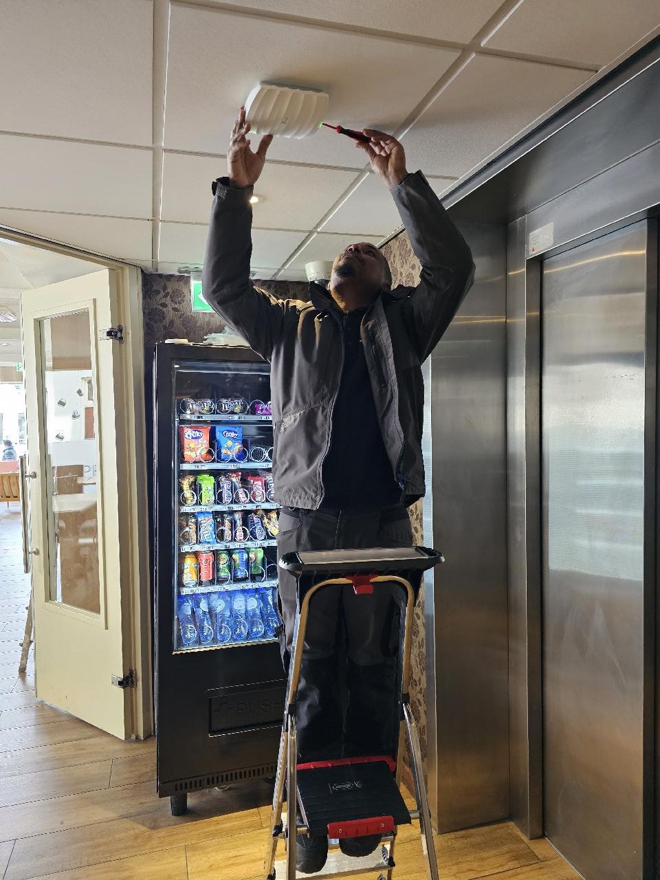 Monteur op een trap hangt een access point aan het plafond van de lobby, naast een automaat