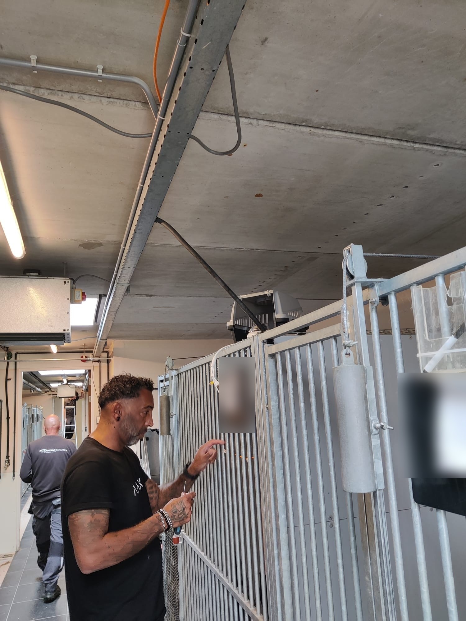 Monteur zet een netwerkkabel af bij een kennel, met de kabelgoot aan het plafond en collega's verderop in de gang