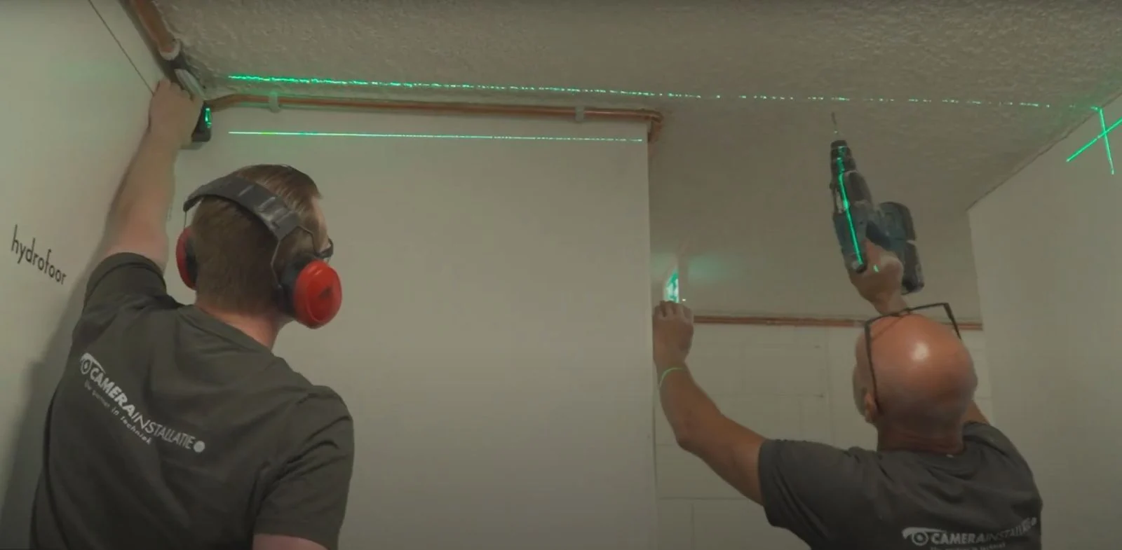Twee monteurs van CameraInstallatie lijnen met een groene laser de camerapositie uit tegen het plafond