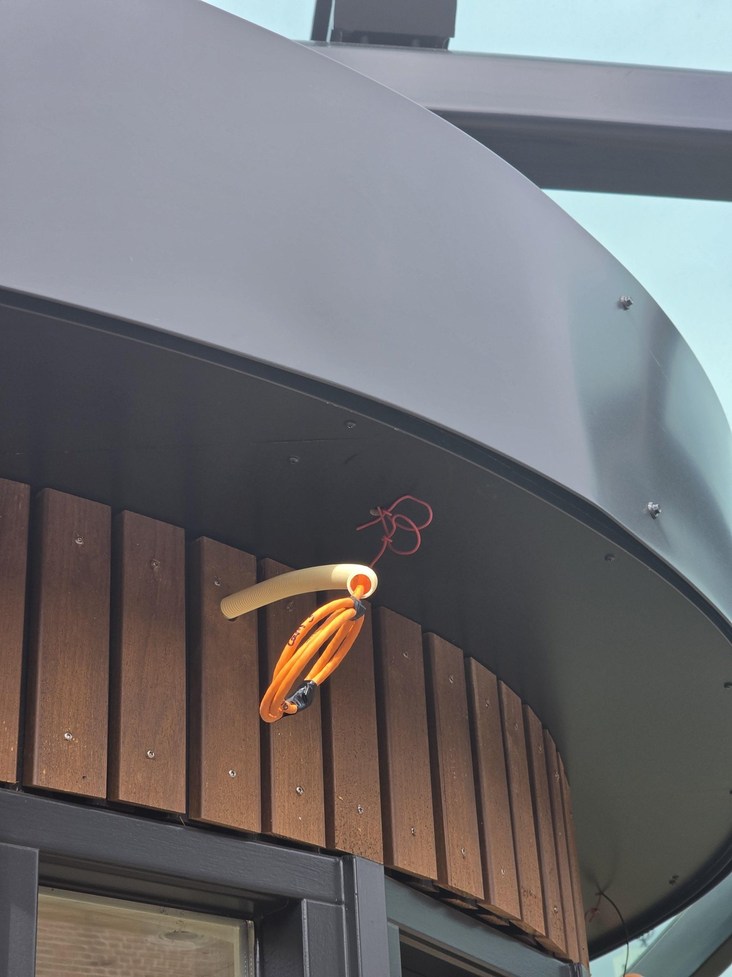 Opgerolde oranje netwerkkabel in een mantelbuis onder de dakrand, klaar voor de camera