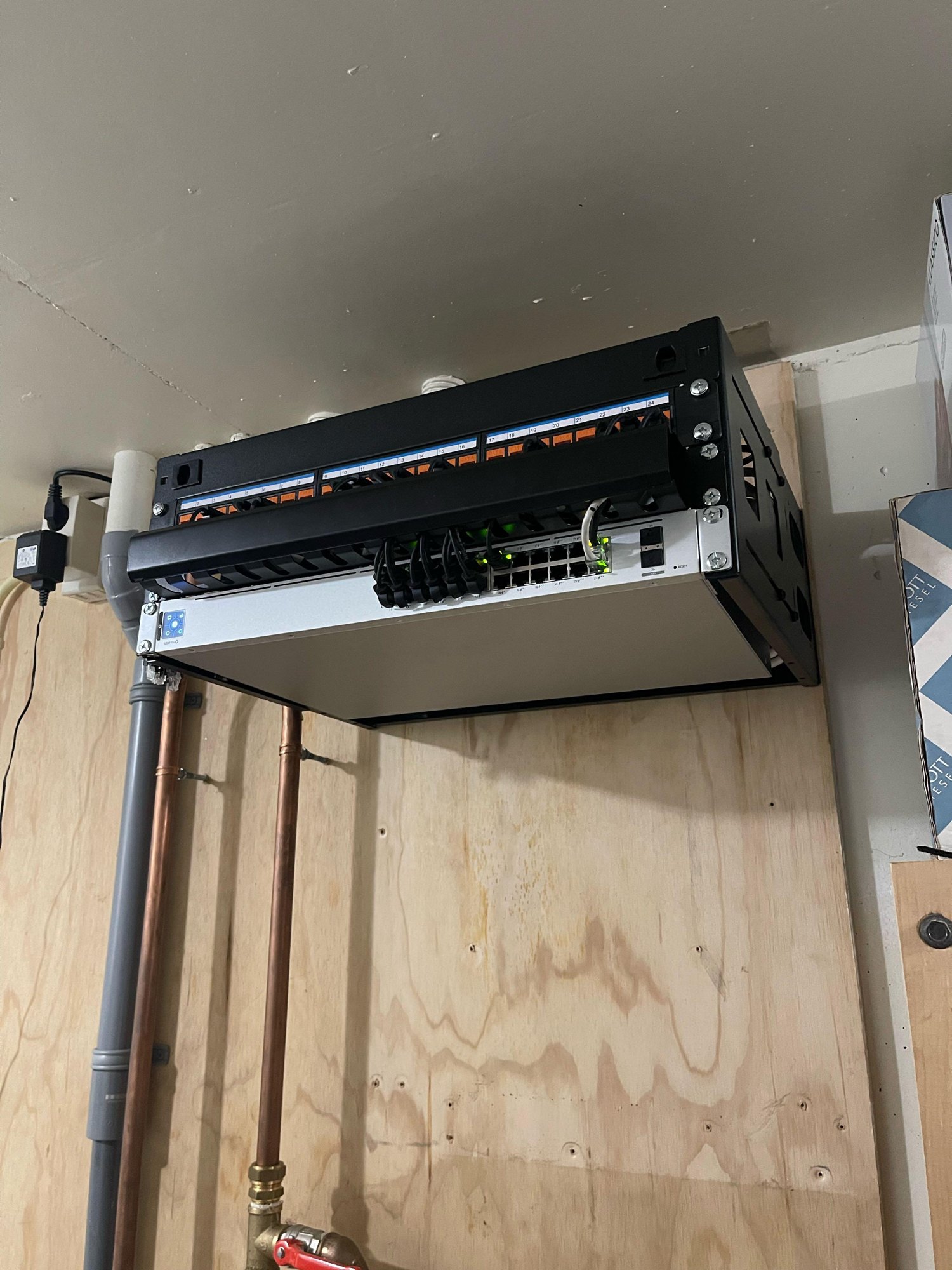 Close-up van het patchrek: genummerde oranje keystones in het rangeerpaneel, korte zwarte patchkabels naar de UniFi-switch met 24 PoE-poorten