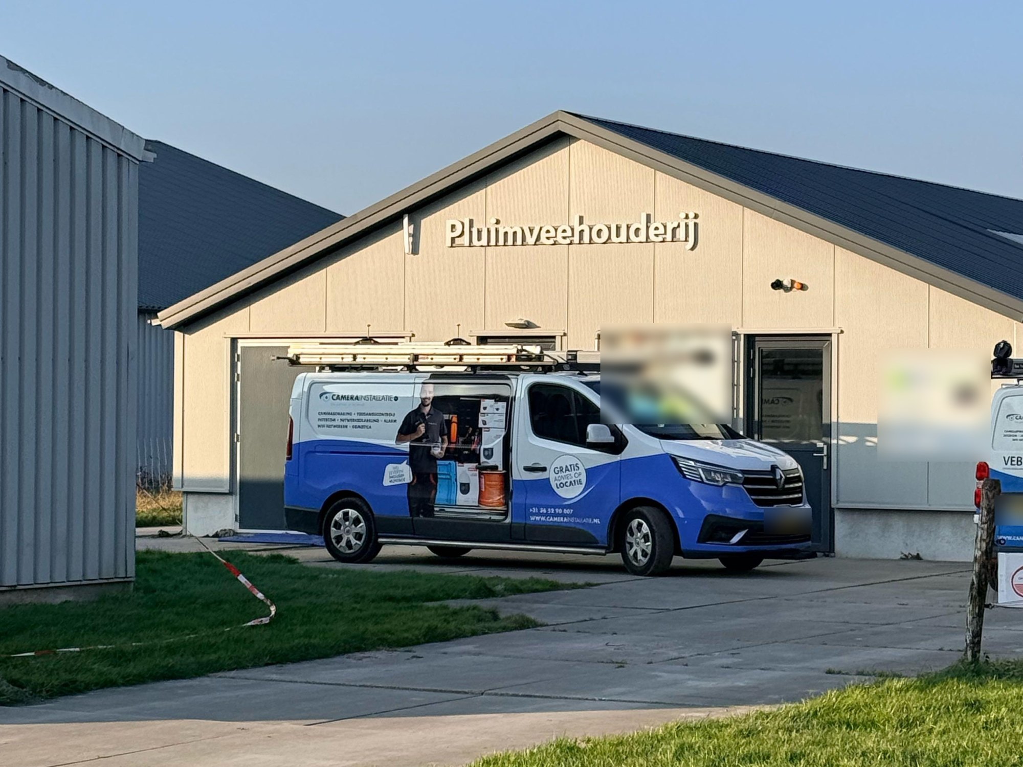 Lichte stal met het opschrift Pluimveehouderij, met de bus van CameraInstallatie.nl ervoor op het erf
