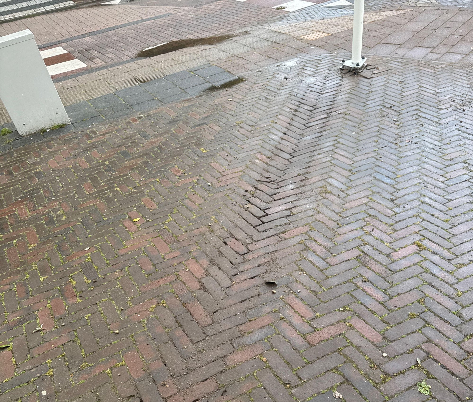 Rode klinkers in visgraatverband op de stoep, met de voet van de witte vlaggenmast op de hoek