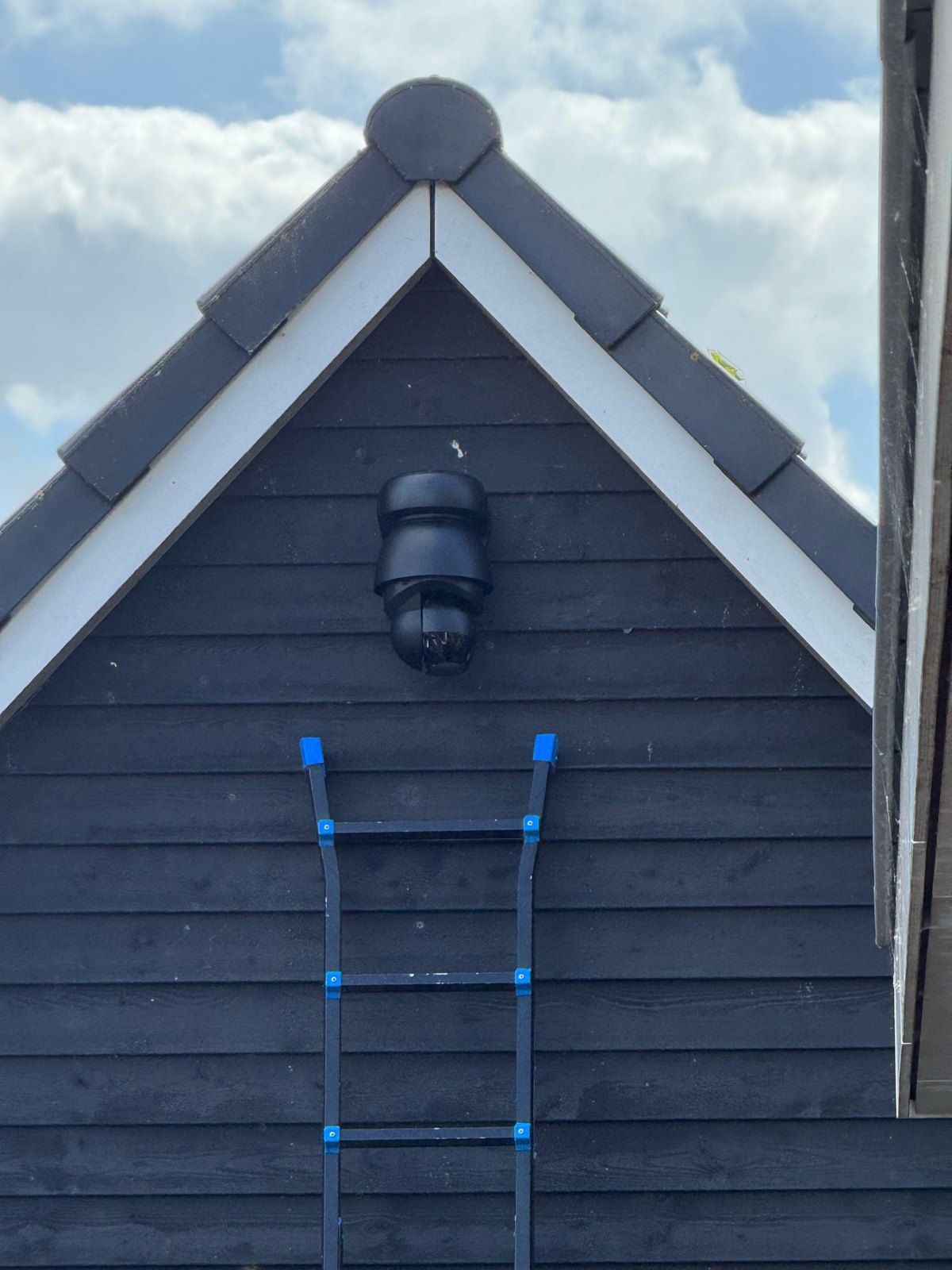 Zwarte draai- en zoomcamera hoog in de nok van een zwarte houten schuur met wit boeiboord