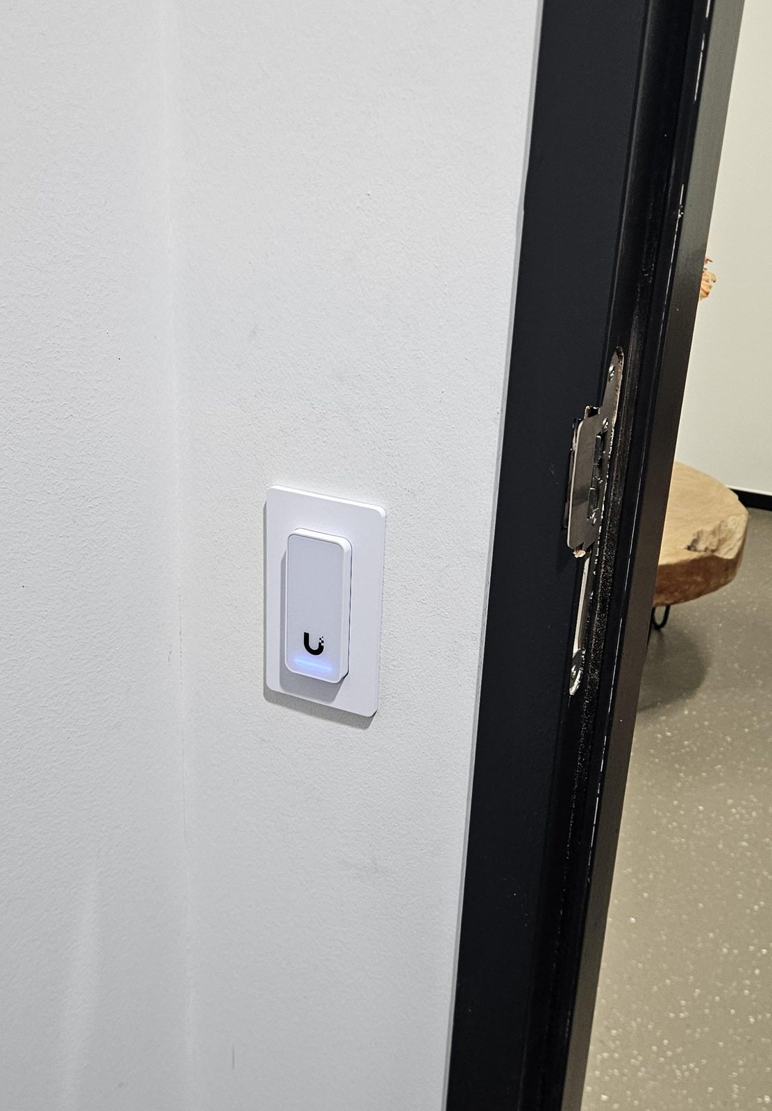 Witte UniFi-lezer met blauw lampje in een gipswand naast een zwart deurkozijn