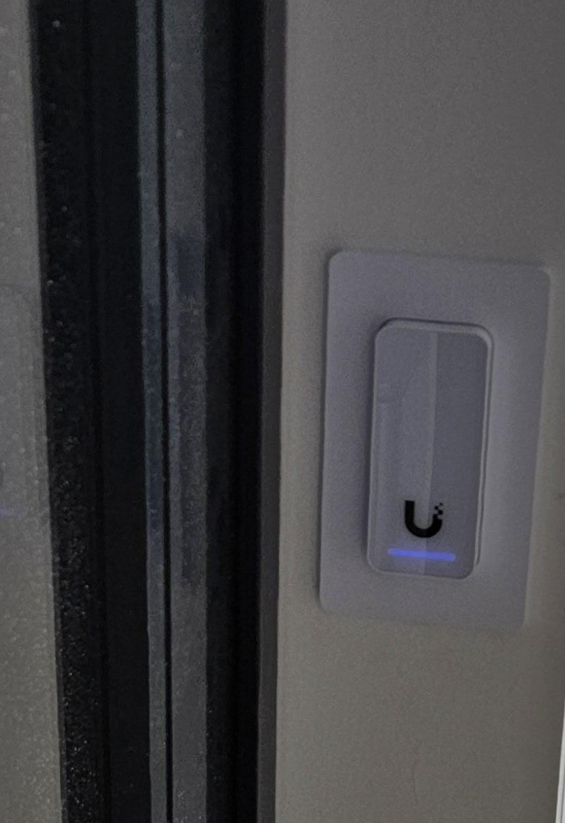 Witte UniFi-lezer met inbouwraam op het kozijn van een glazen pui