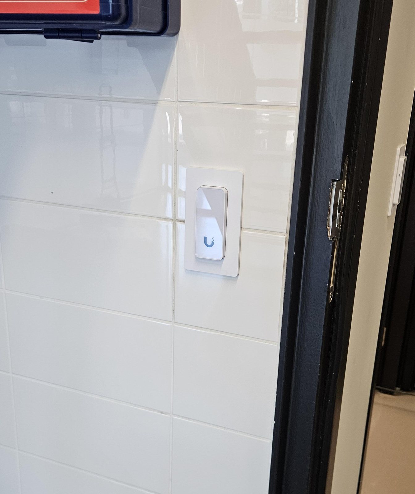Witte UniFi-toegangslezer ingebouwd in witte wandtegels naast een zwart deurkozijn