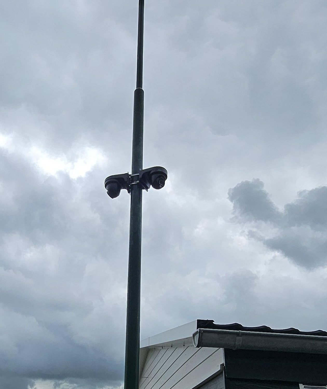 Twee zwarte turretcamera’s aan een beugel rond een mast, tegen een grijze lucht