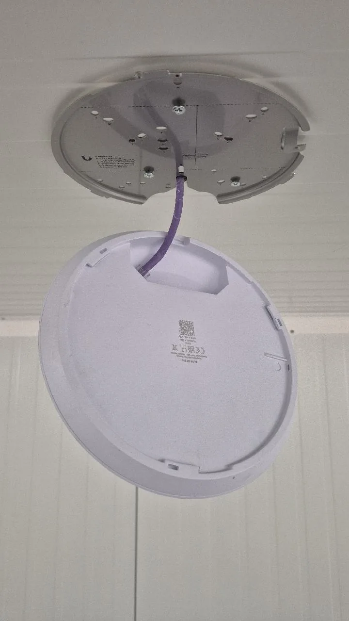 Montageplaat van een UniFi-access point aan het plafond met de paarse datakabel erdoor