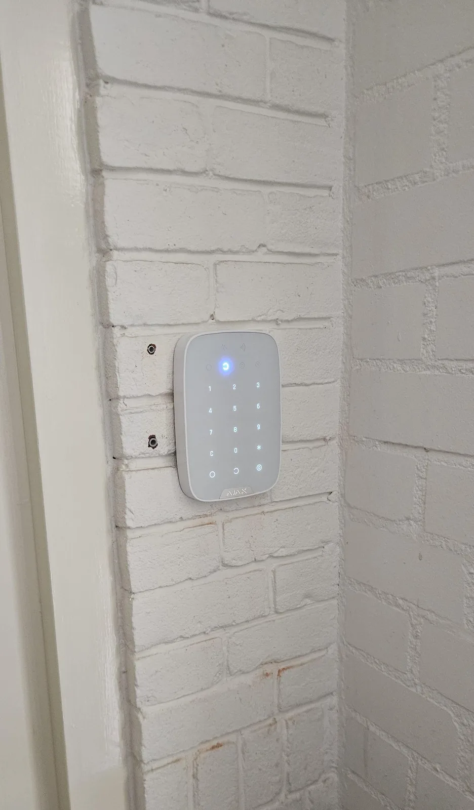 Wit Ajax-keypad op een witgeschilderde bakstenen muur naast de deur, bij een woning in Zeist