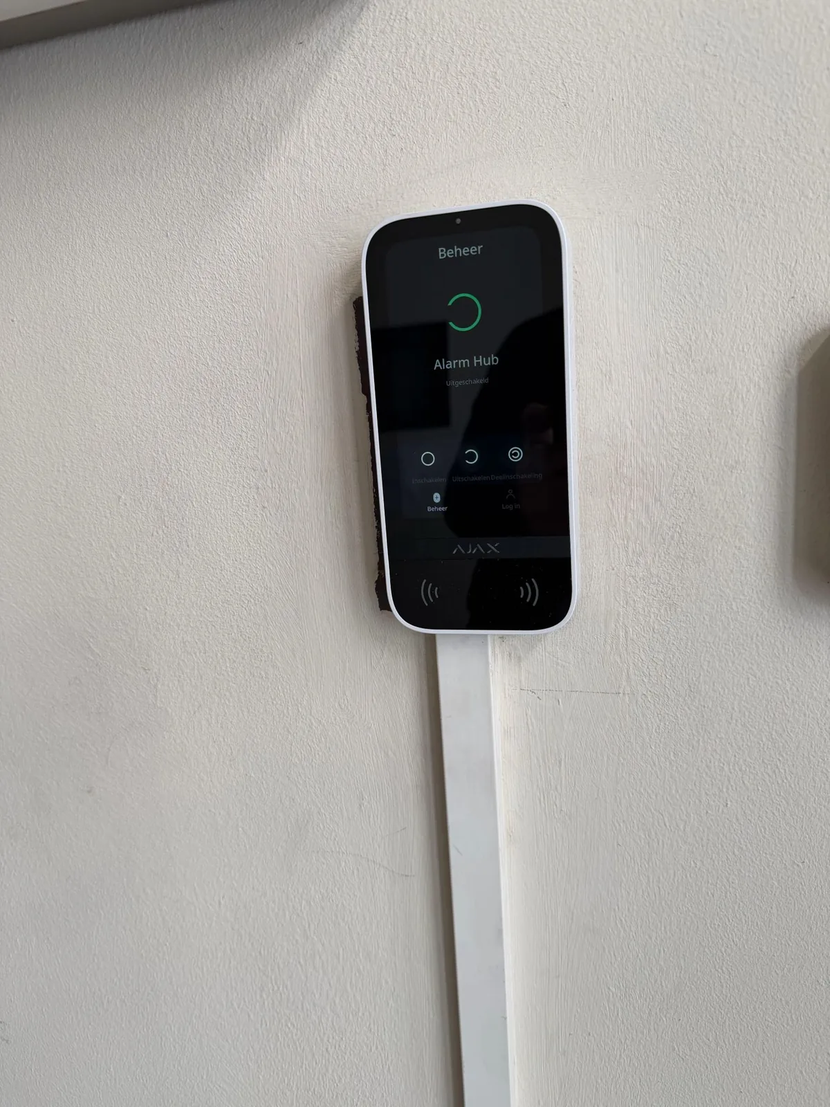Wit Ajax KeyPad TouchScreen op een witte wand, met op het scherm Alarm Hub