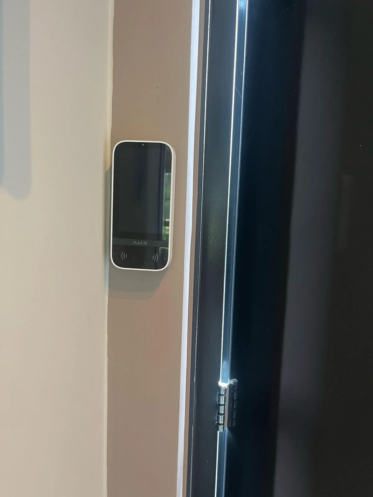 Witte Ajax Superior KeyPad TouchScreen op een lichte wand naast een zwarte deur