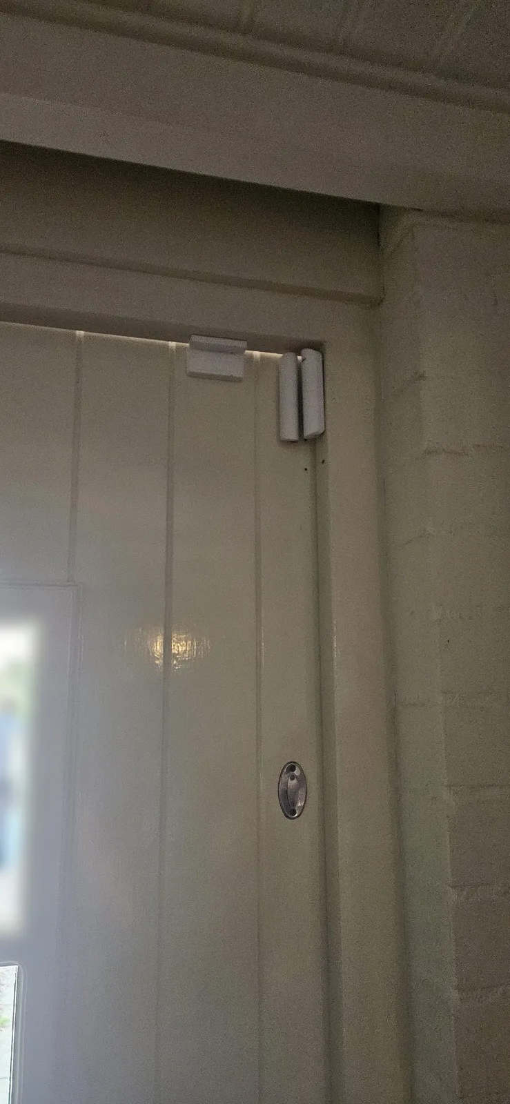 Wit Ajax-magneetcontact boven in de hoek van een crèmekleurige deur met glas