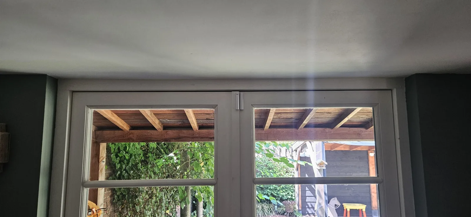 Wit Ajax-magneetcontact boven op dubbele tuindeuren, met zicht op de pergola
