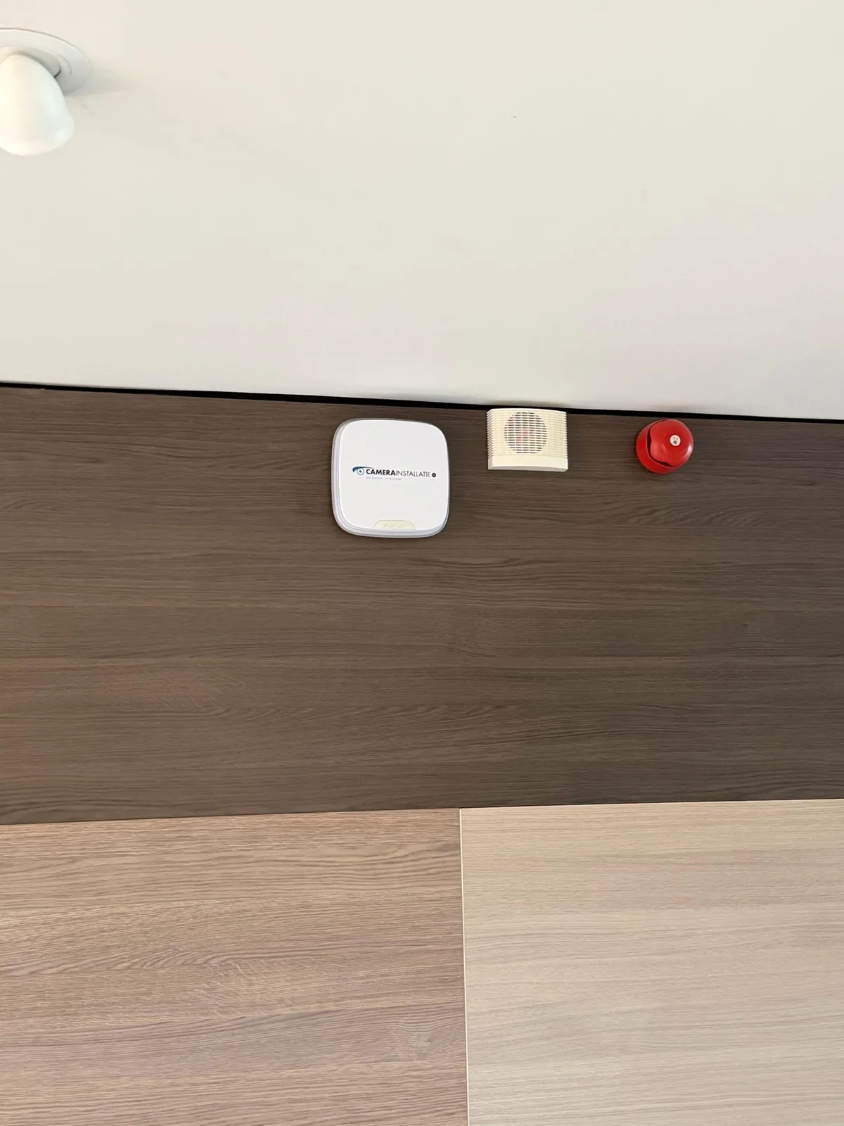 Witte Ajax-sirene met het logo van CameraInstallatie.nl op een donkere houten wand