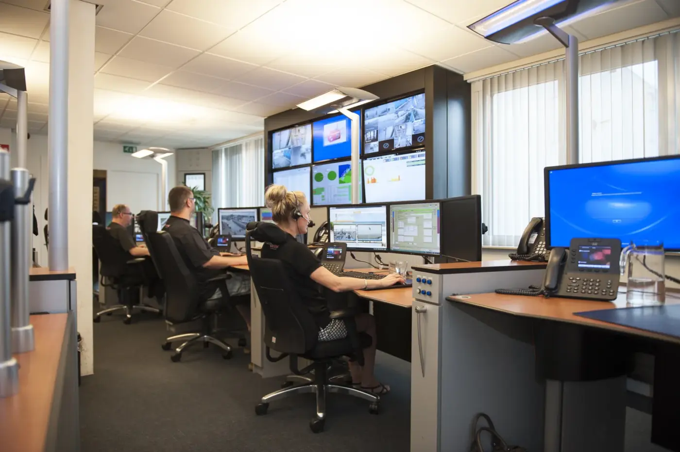 Centralisten met headset aan werkplekken in de meldkamer van Alarm Control Nederland