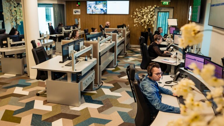 Centralisten met headset aan werkplekken in de meldkamer van Alarm Meldnet