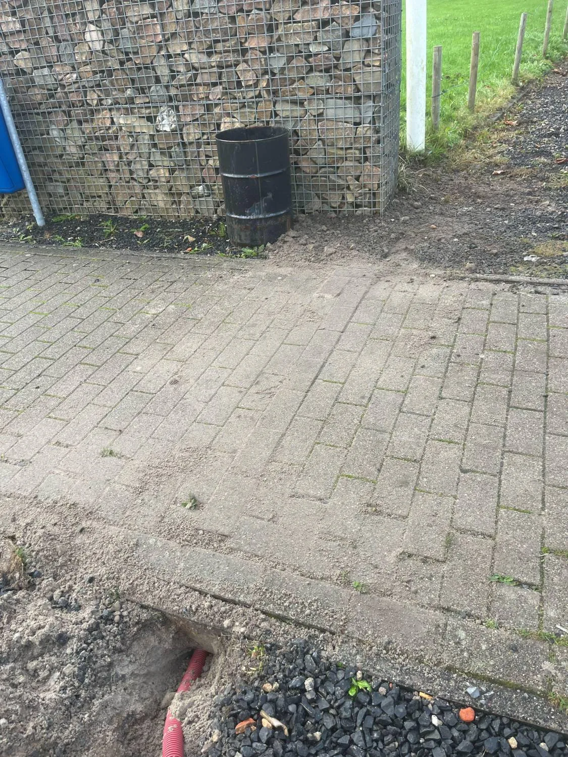 Teruggelegde bestrating over een kabelsleuf, met op de voorgrond de rode buis in de grond
