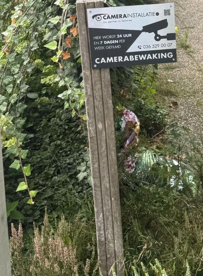 Bord camerabewaking van CameraInstallatie.nl op een houten paal naast een pad