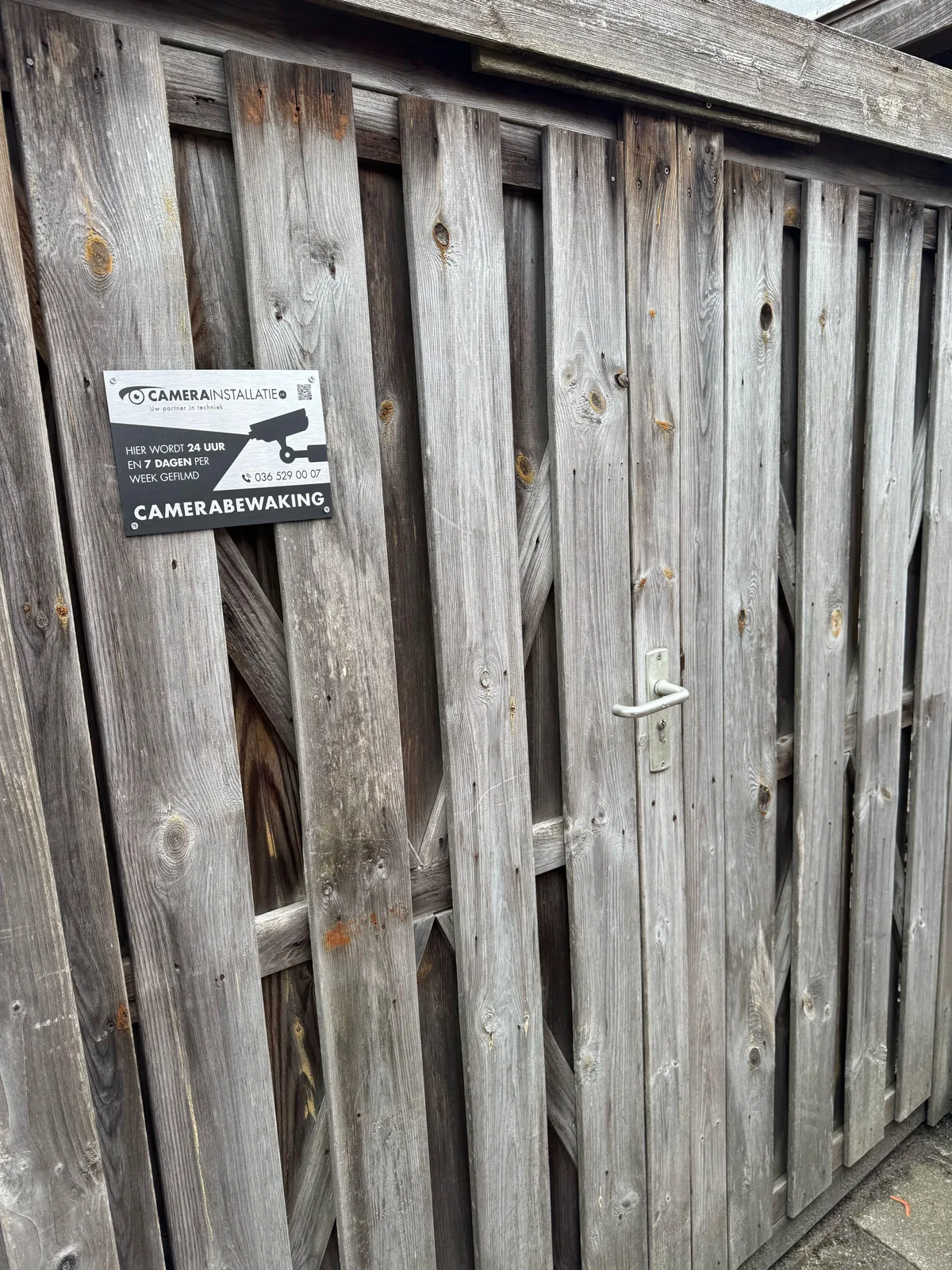 Bord camerabewaking van CameraInstallatie.nl op een houten tuinpoort