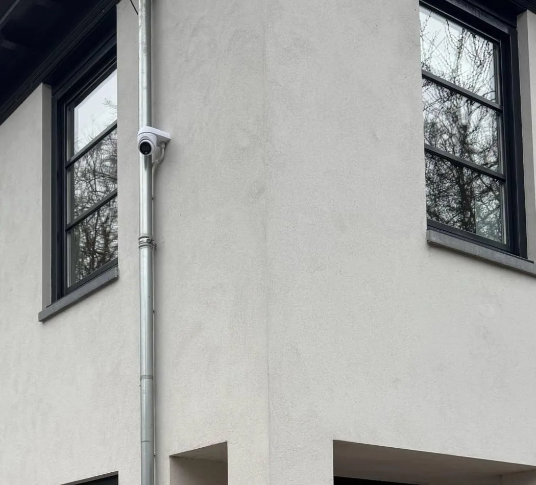 Witte camera hoog aan een witte gevel, naast de ramen van de woning