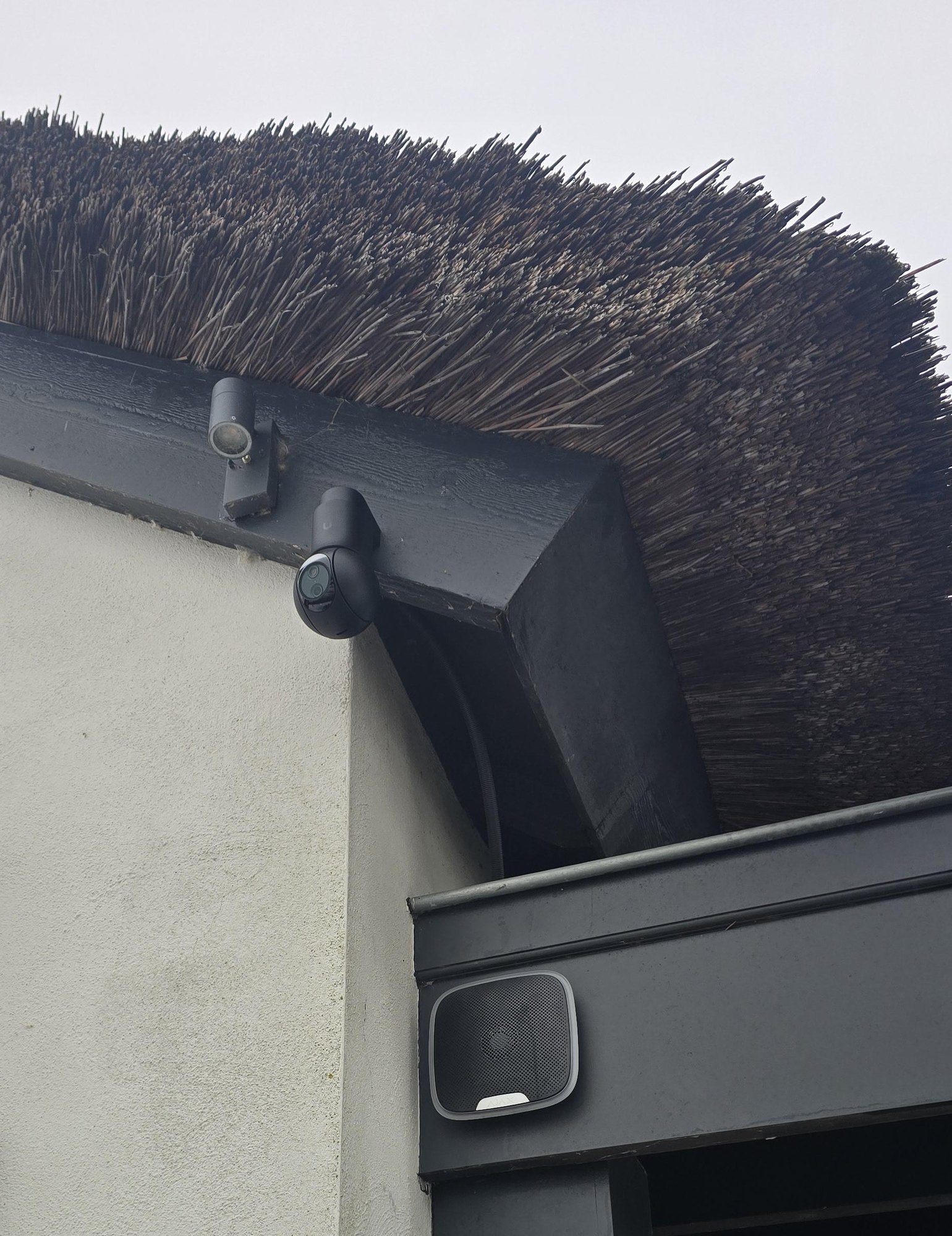 Zwarte camera onder de rand van een rieten kap, met daaronder een wifi-zender bij de overkapping