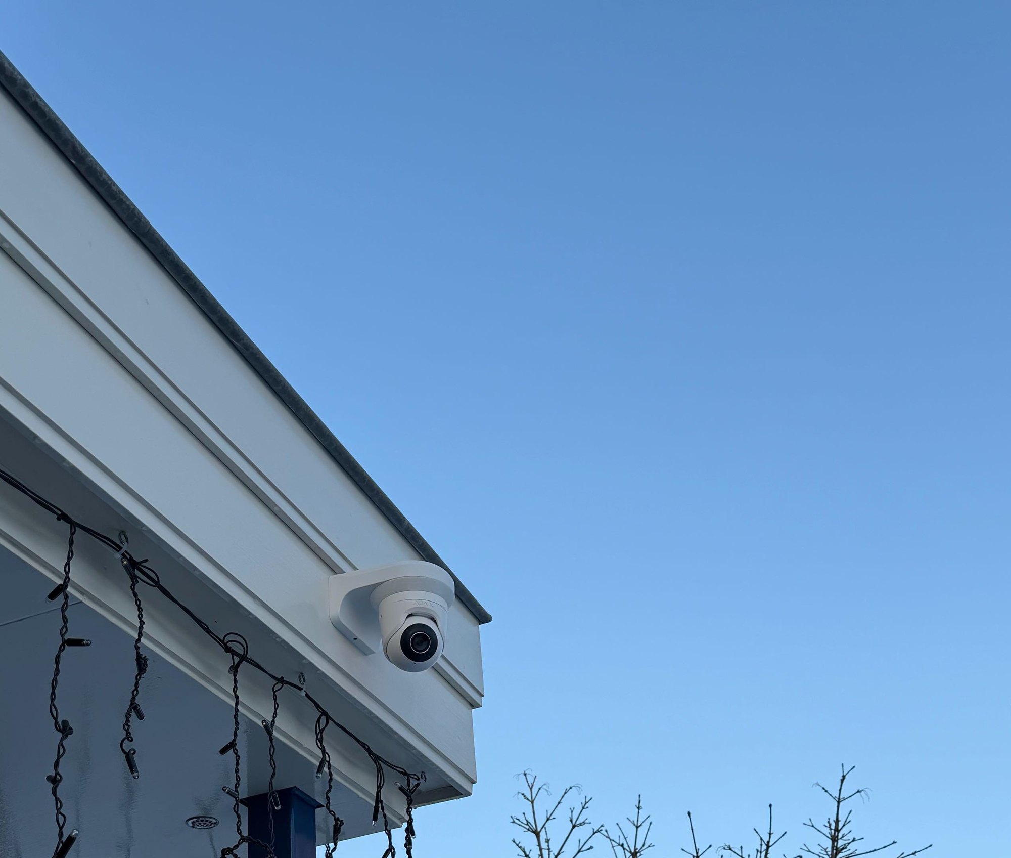 Witte camera op de hoek van een witte dakrand, tegen een strakblauwe winterlucht