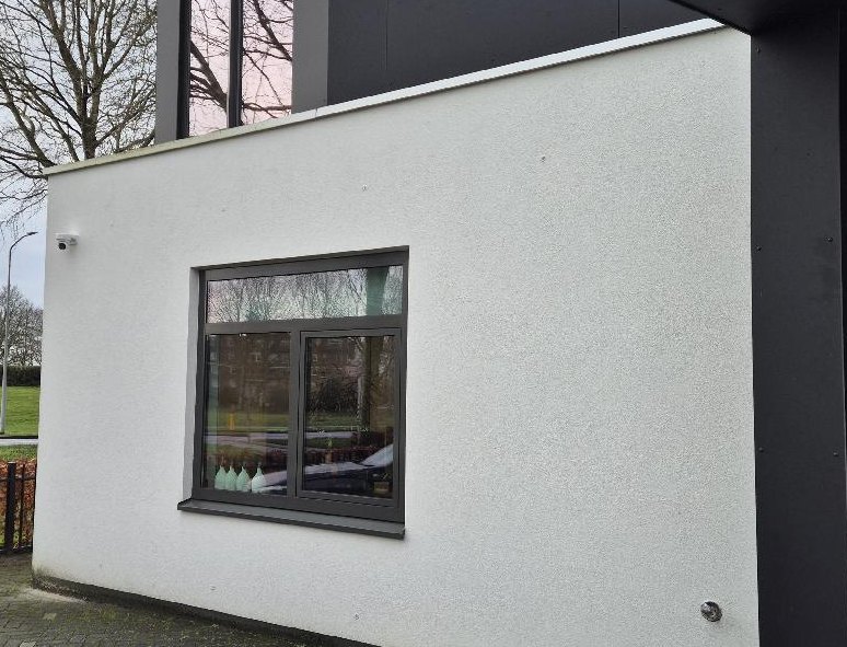 Witte aanbouw met een raam, met een kleine witte camera op de hoek onder de dakrand