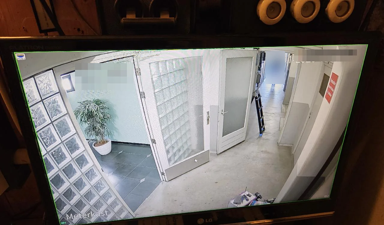Live beeld op de monitor: de centrale hal met de deuren en de gang, groot in beeld