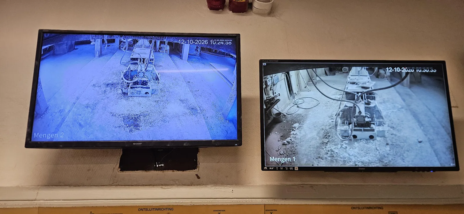 Twee schermen in de controlekamer met live camerabeeld van Mengen 1 en Mengen 2