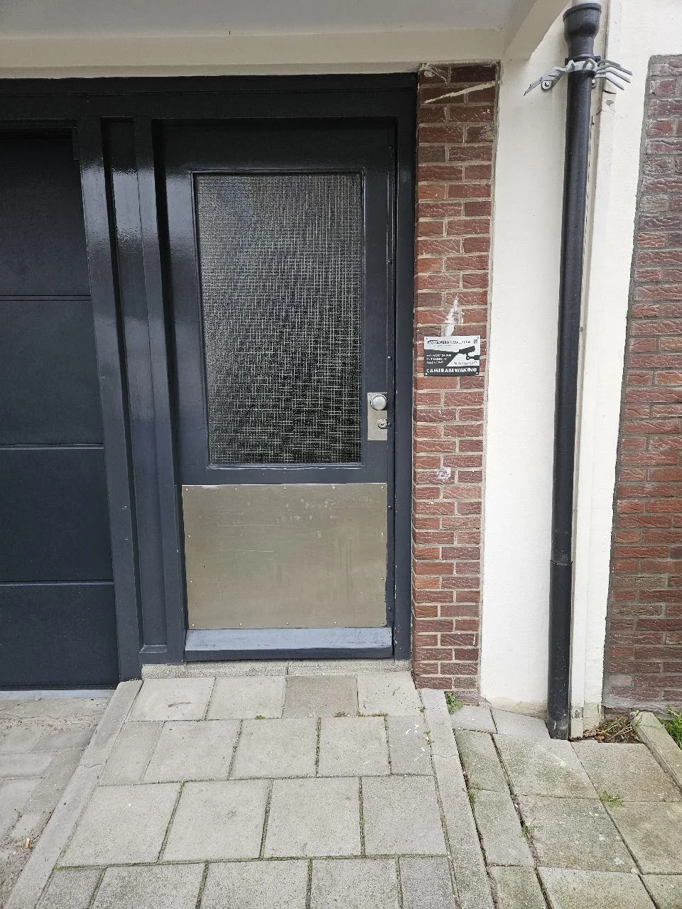 Bordje camerabewaking naast de tweede toegangsdeur, tussen de deur en de regenpijp
