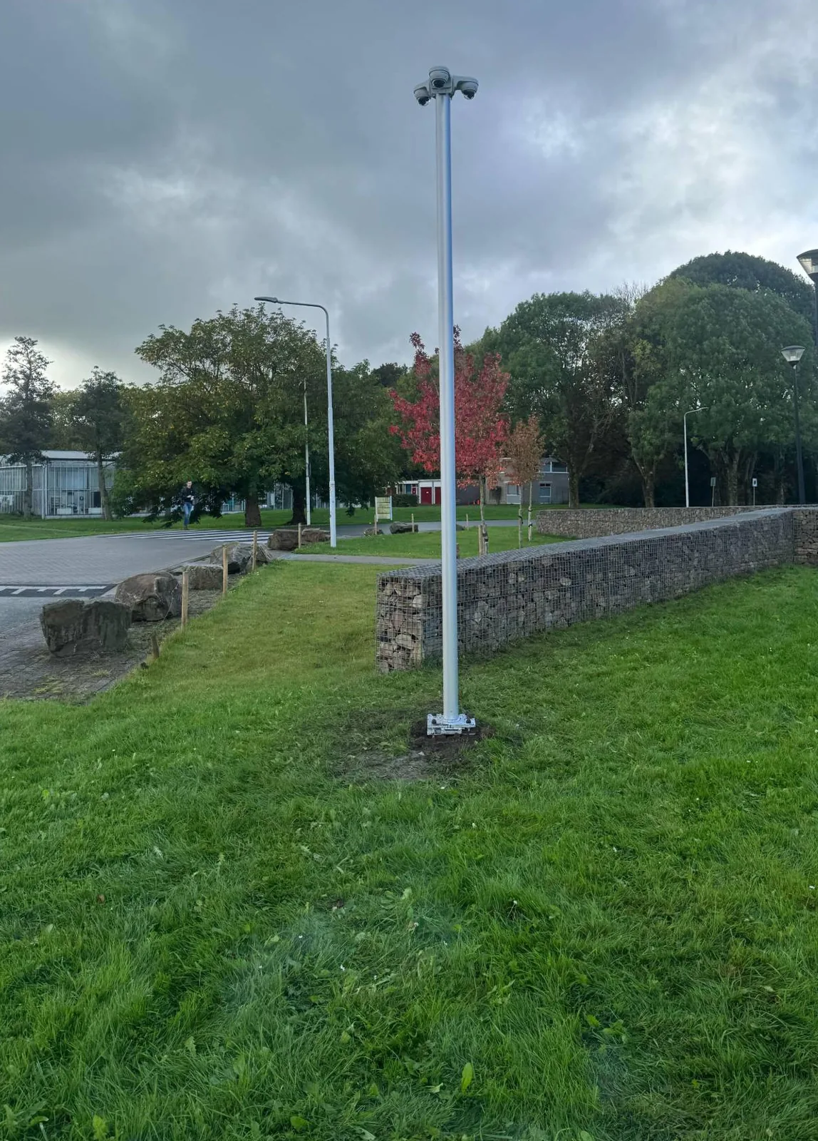 Vaste camerapaal met drie camera’s op een grasveld naast een schanskorf, bij een school