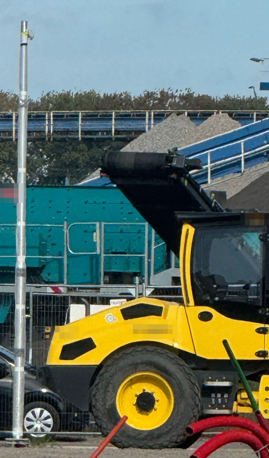 Camerapaal in beschermfolie op een bouwterrein, naast een gele wals en een zeefinstallatie
