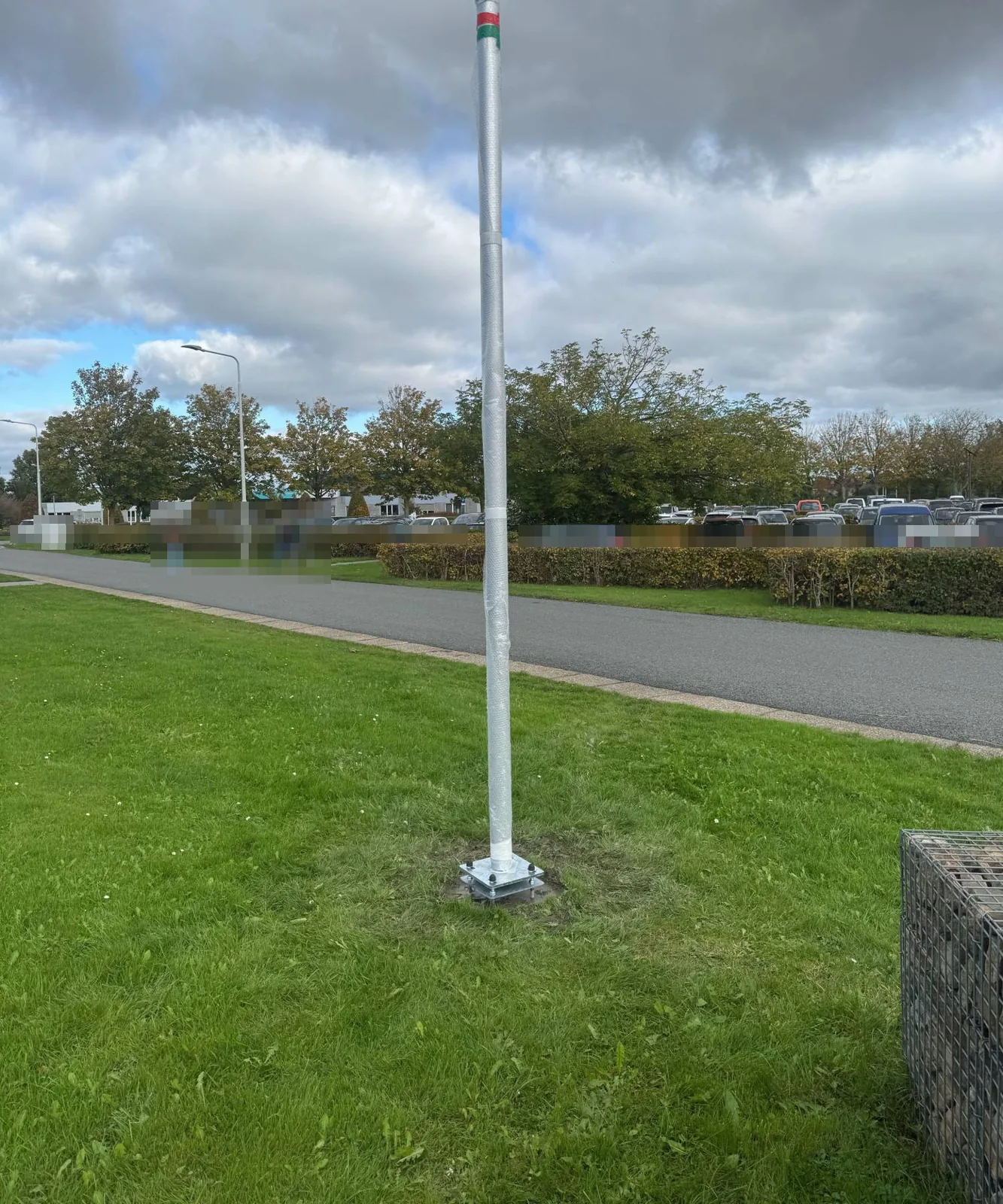 Net geplaatste camerapaal in beschermfolie op een grasveld langs een weg op een schoolterrein