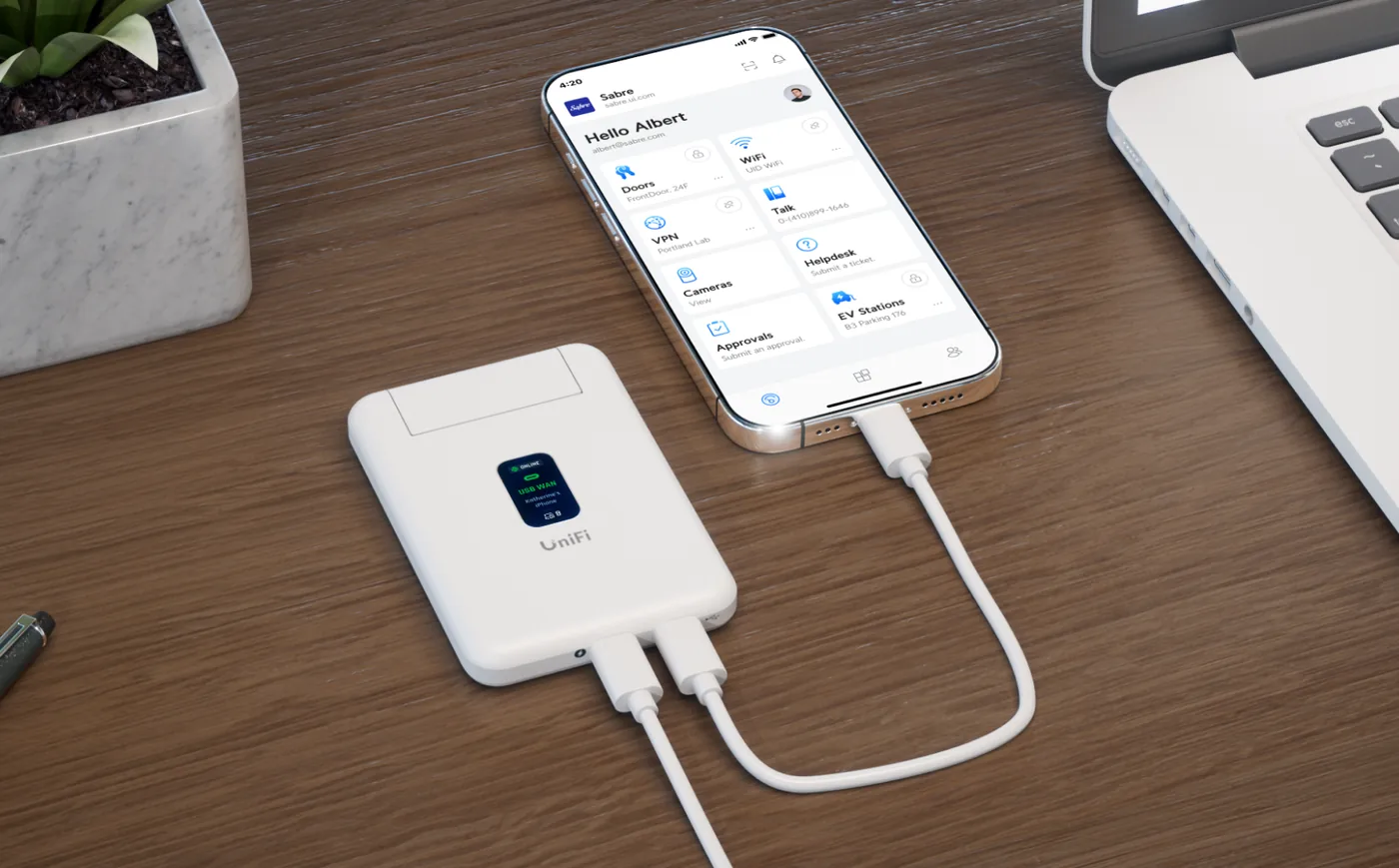 UniFi Travel Router op een houten bureau, met een USB-kabel aangesloten op een telefoon