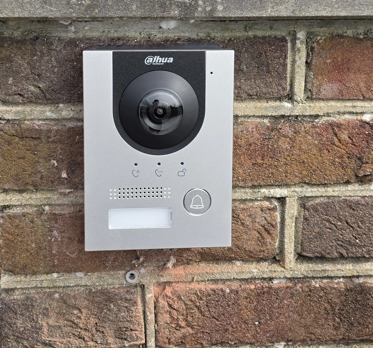 Dahua-buitenpost van dichtbij, met de fisheye-camera, de belknop en een leeg naambordje, vastgezet op het metselwerk van de pilaar