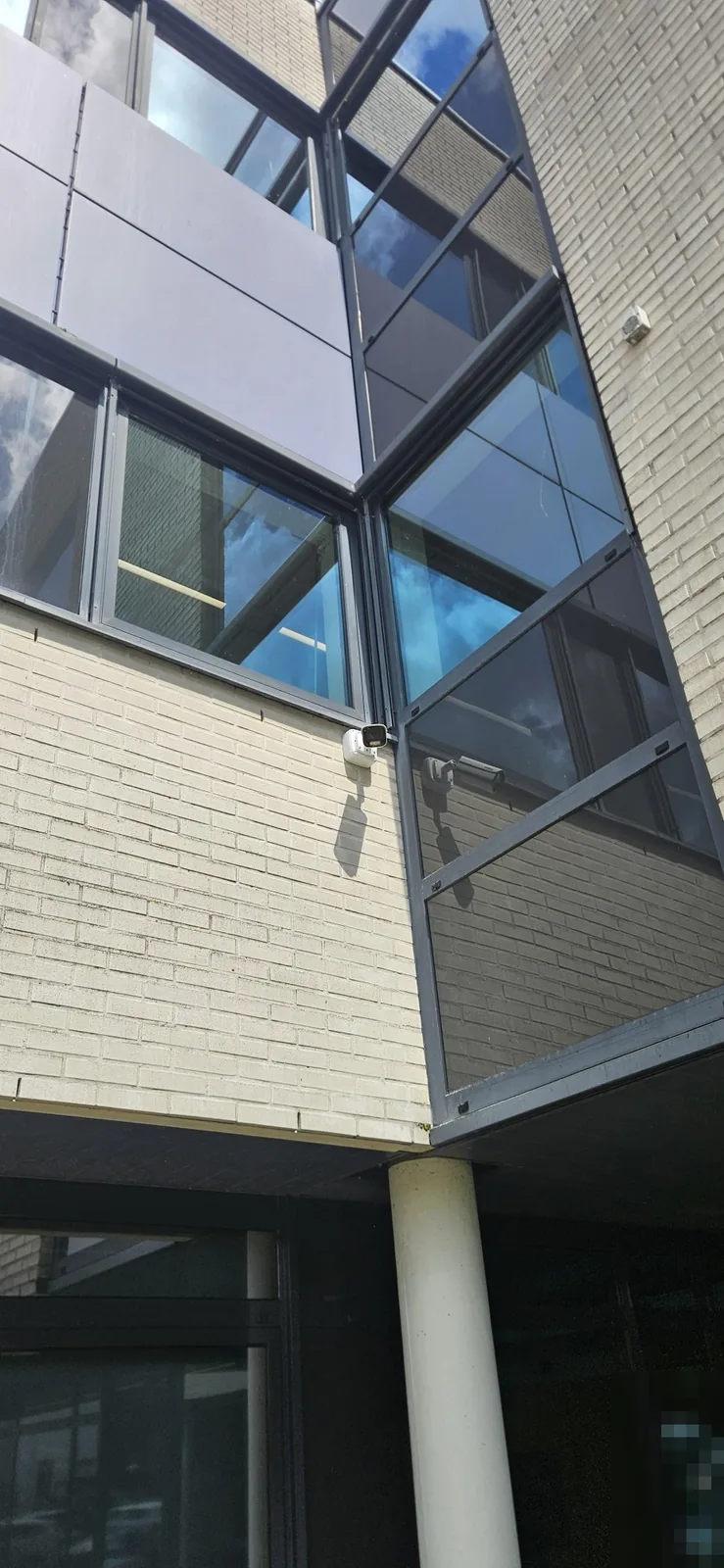 Witte Dahua-bulletcamera op de gevel van lichte baksteen, naast een glazen trappenhuis