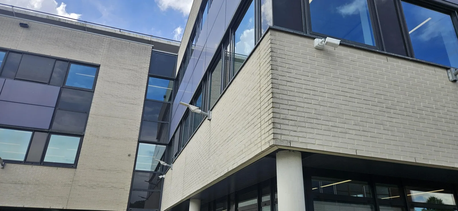 Witte Dahua-bulletcamera op een muurbeugel op de hoek van een kantoorgevel van lichte baksteen