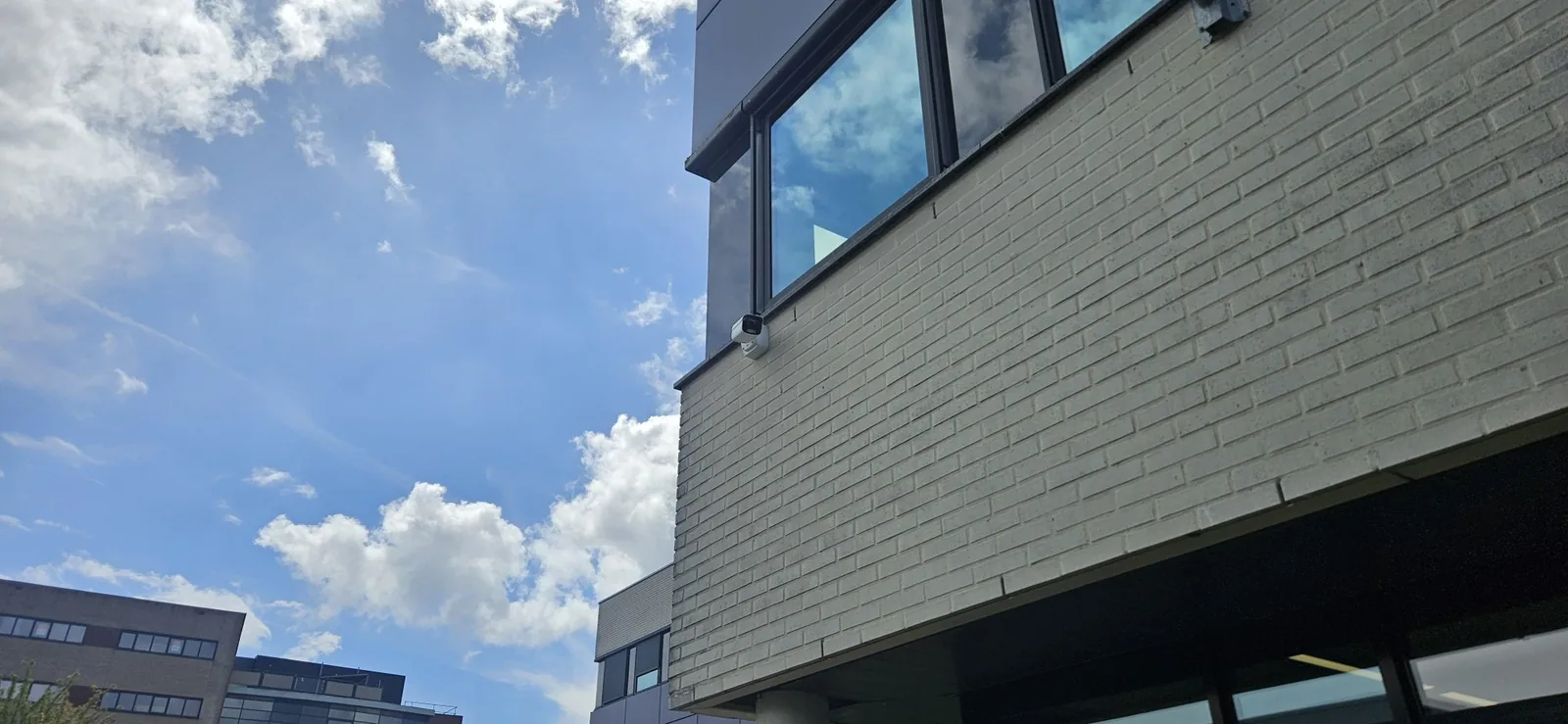 Witte Dahua IPC-HFW5859E1-ZE-IL op een muurbeugel tegen lichte baksteen