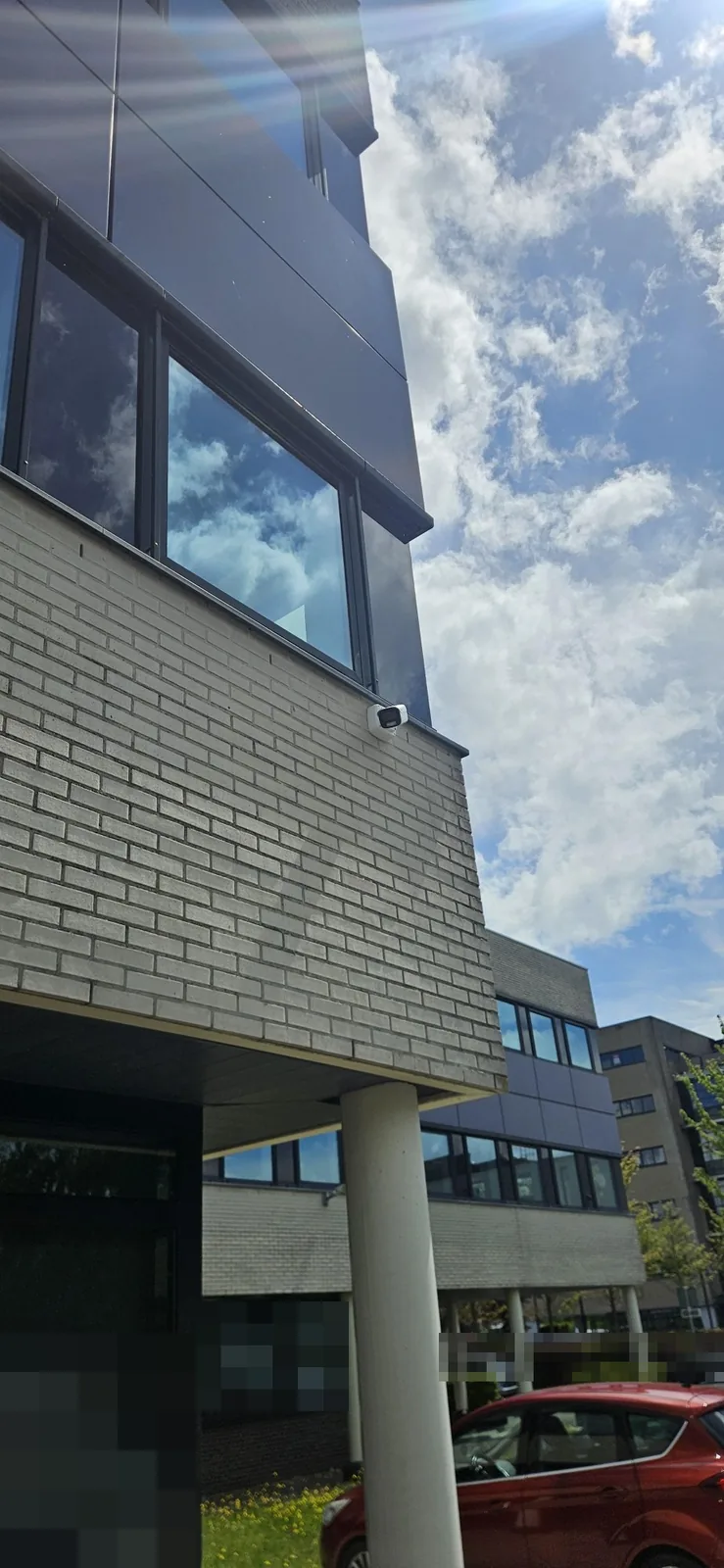 Witte Dahua-bulletcamera op een muurbeugel onder een raam van een kantoorgevel van lichte baksteen