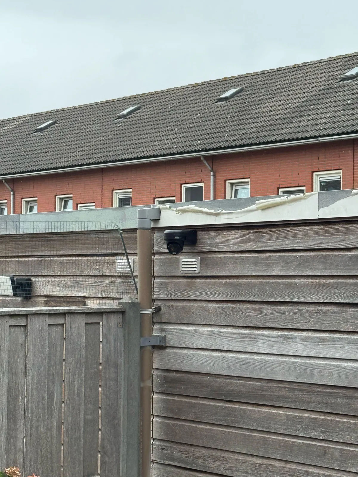 Zwarte Dahua-camera op de houten schuur in de achtertuin, iets omhoog gericht op het afdak