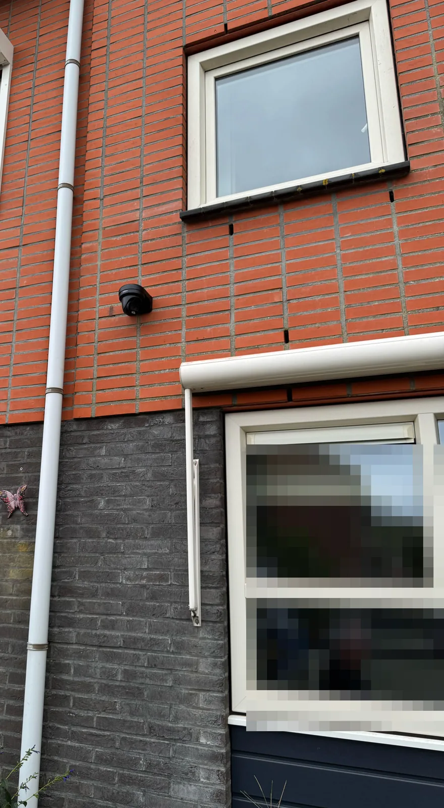 Zwarte Dahua-camera op de voorgevel tussen de ramen, naast de witte regenafvoer