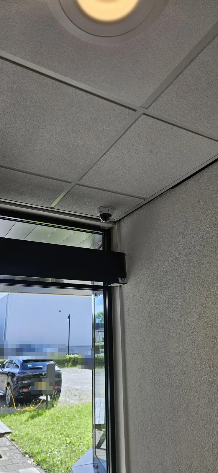 Dahua-domecamera aan het plafond van de hal, boven de glazen buitendeur