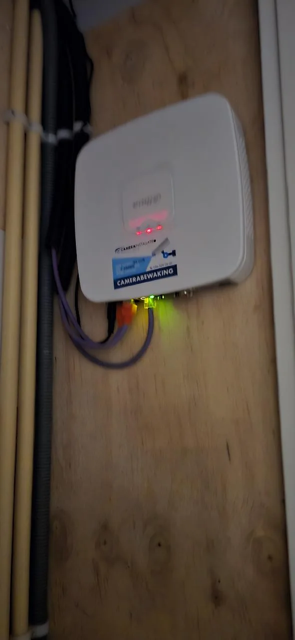 Witte Dahua-recorder voor vier camera’s op een houten plaat in de meterkast, met netwerkkabels en buizen ernaast