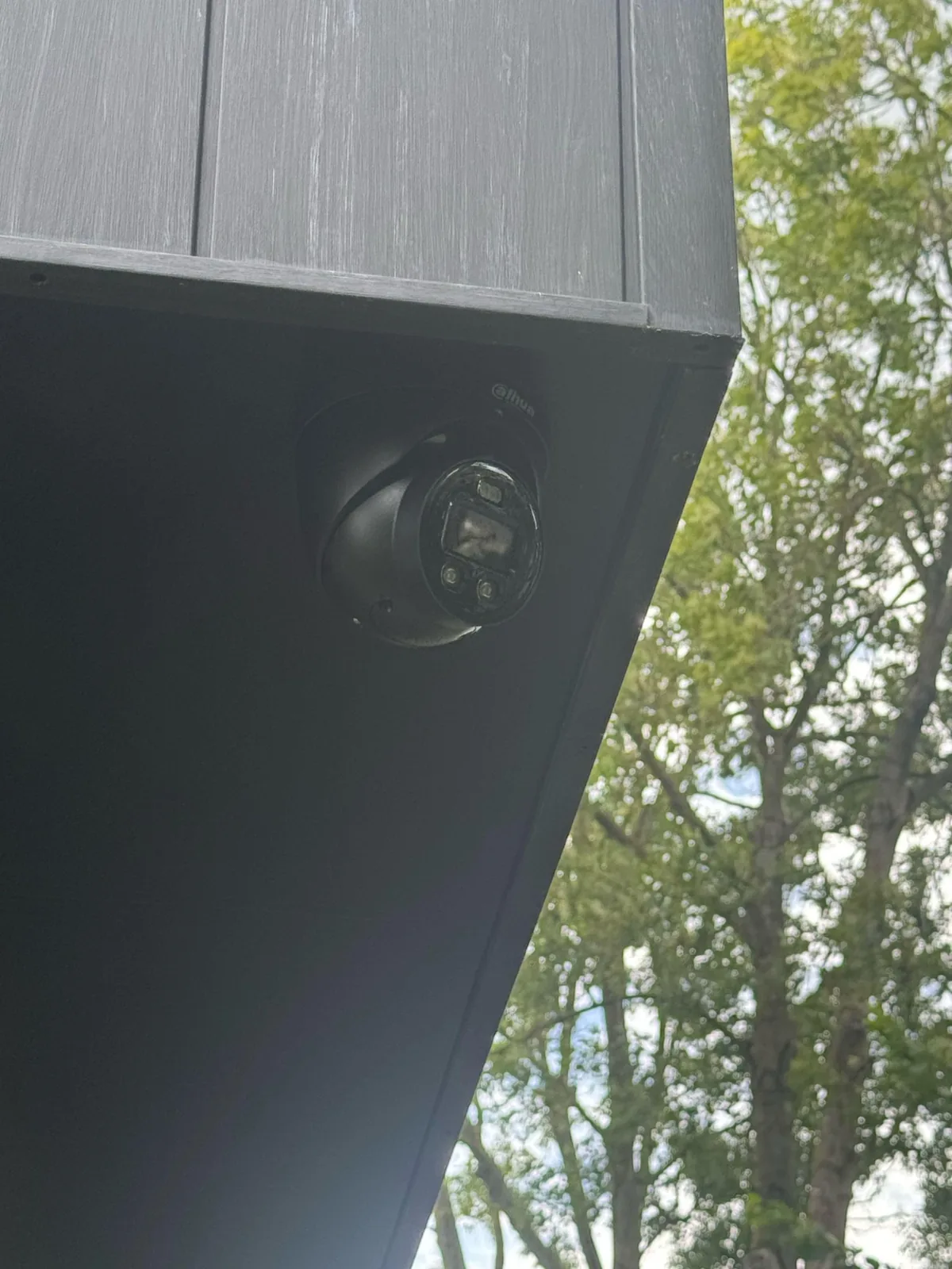 Zwarte Dahua TiOC-camera op een zwarte beugel onder het overstek, met bomen op de achtergrond