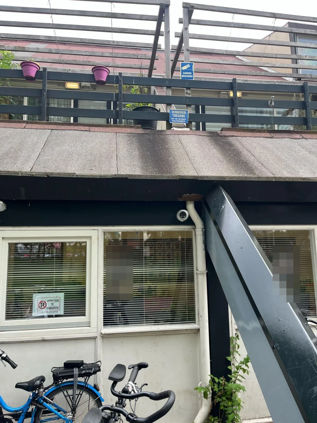 Witte Dahua-turret onder de dakrand bij een schuine balk, met op het balkon erboven een bord camerabewaking