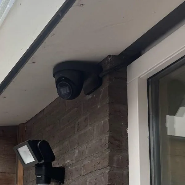 Detail van de zwarte Dahua-turret onder de overkapping, met de kabel in een zwarte flexibele buis langs de balk