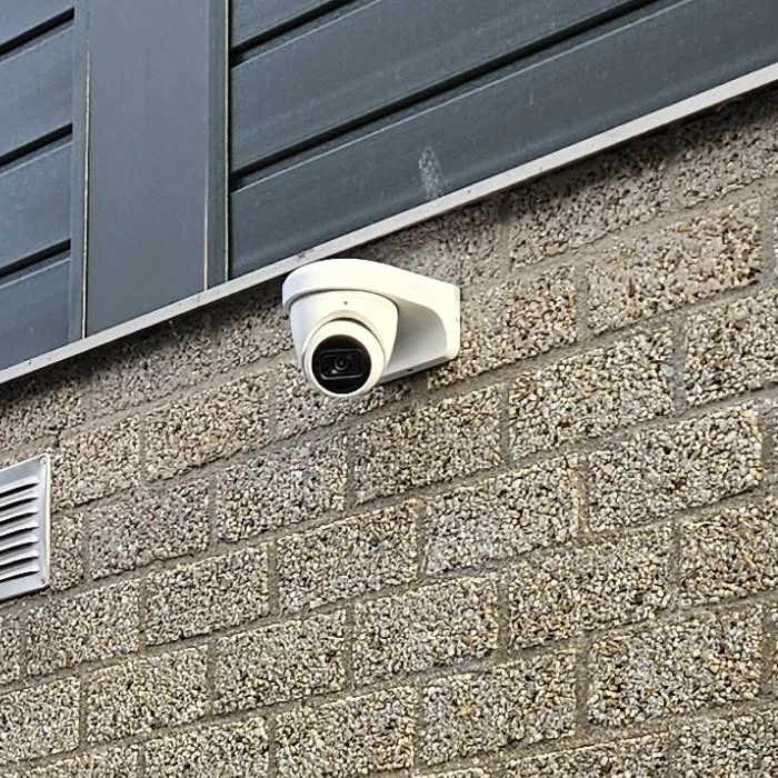 Witte Dahua-turretcamera op een muurbeugel, vlak onder de donkergrijze houten gevelbekleding