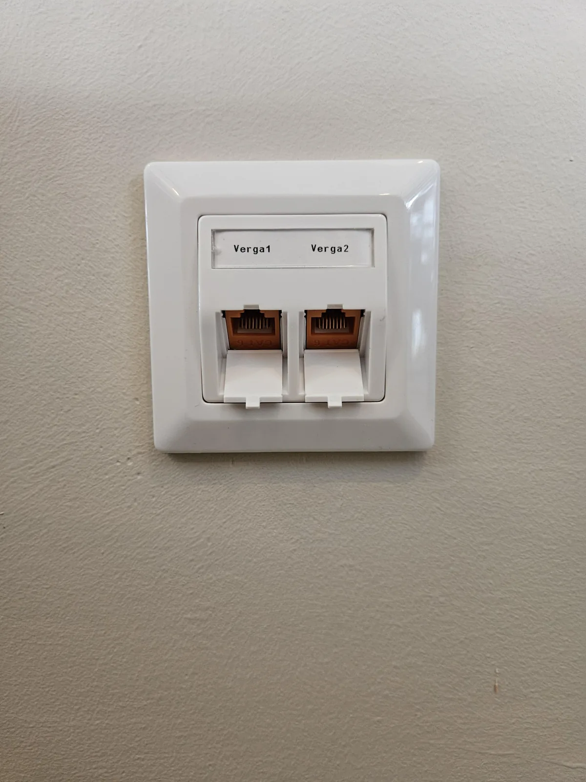 Witte faceplate met twee netwerkpoorten, gelabeld Verga1 en Verga2, in de wand van een vergaderruimte in Amsterdam