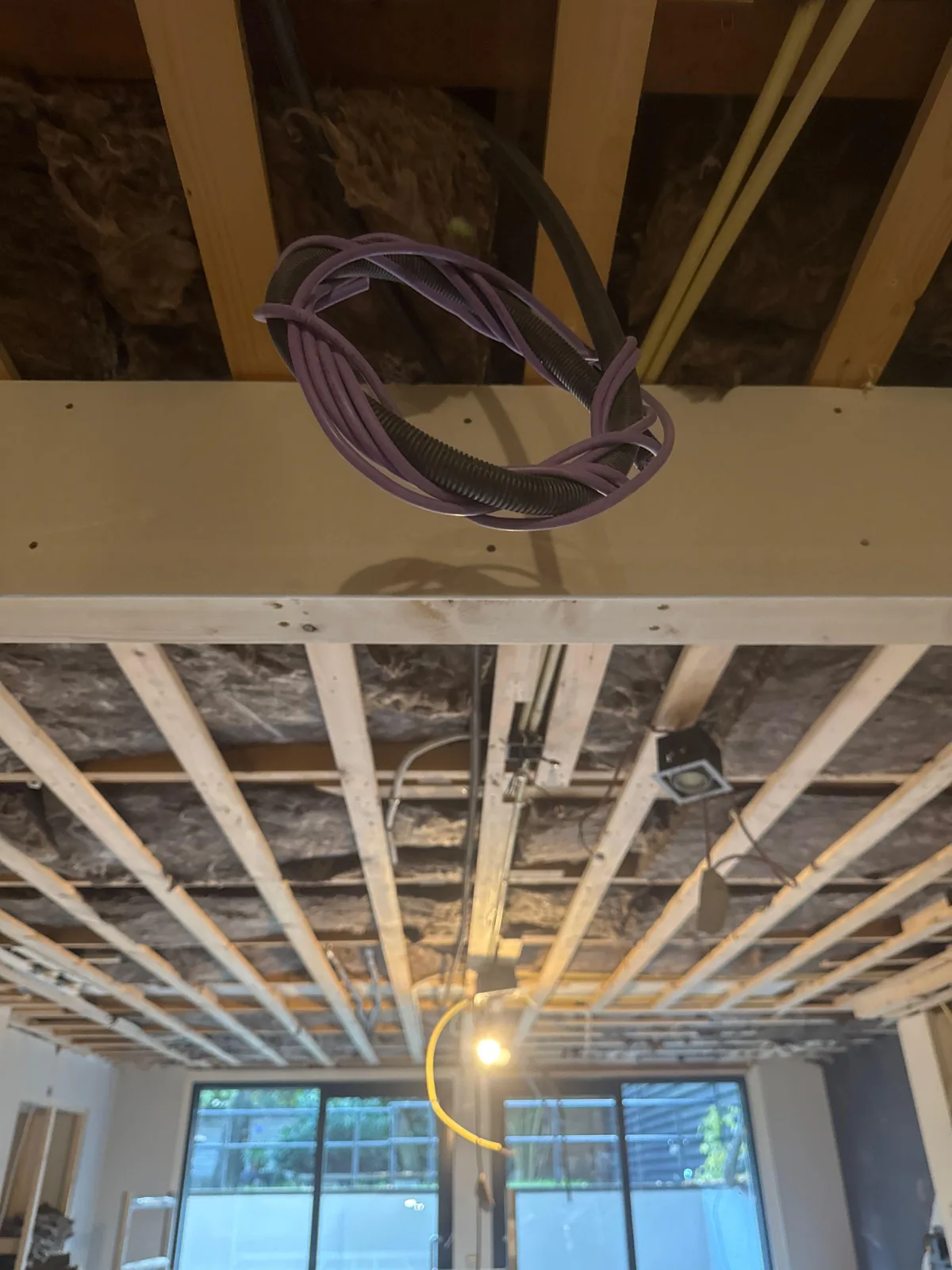 Opgerolde paarse netwerkkabel en zwarte flexbuis die uit een open plafond hangen, klaar voor een access point